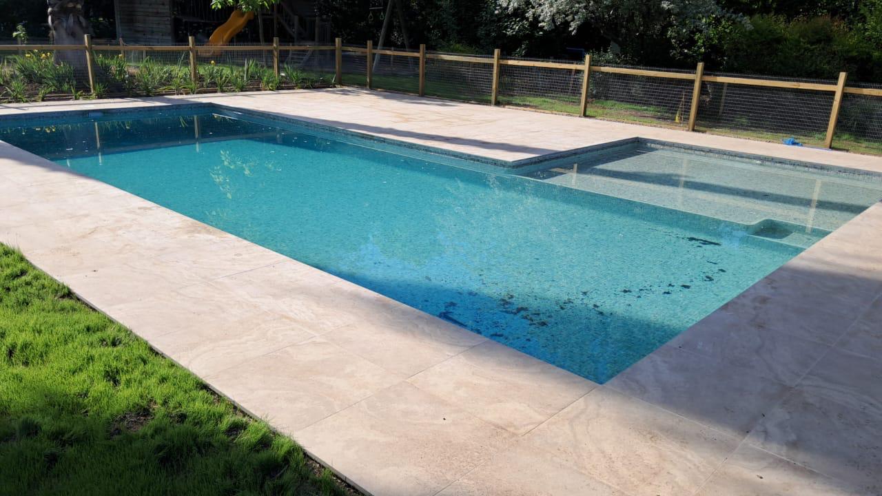 Piscina de hormigón con revestimiento tipo mosaico y borde de travertino construida por Valcorp