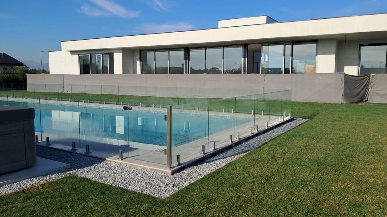 Piscina de gran formato con cierre perimetral de cristal templado frente a casa en obra