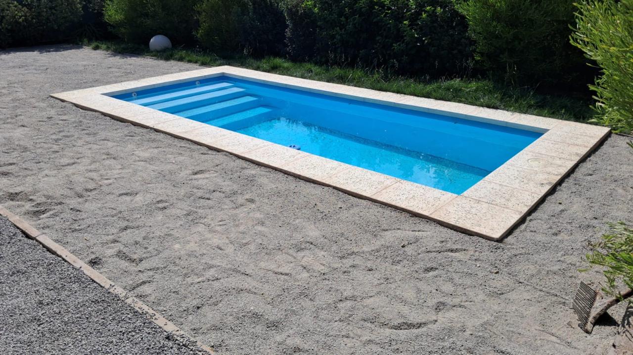 Piscina de fibra de vidrio azul con borde de piedra reconstituida y escalones interiores