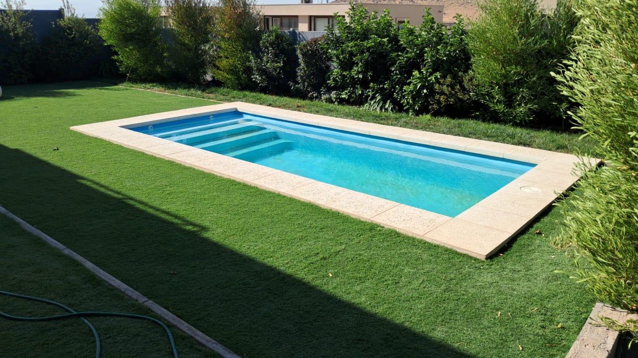 Piscina de fibra de vidrio celeste con escalones y borde de piedra, instalada por Valcorp