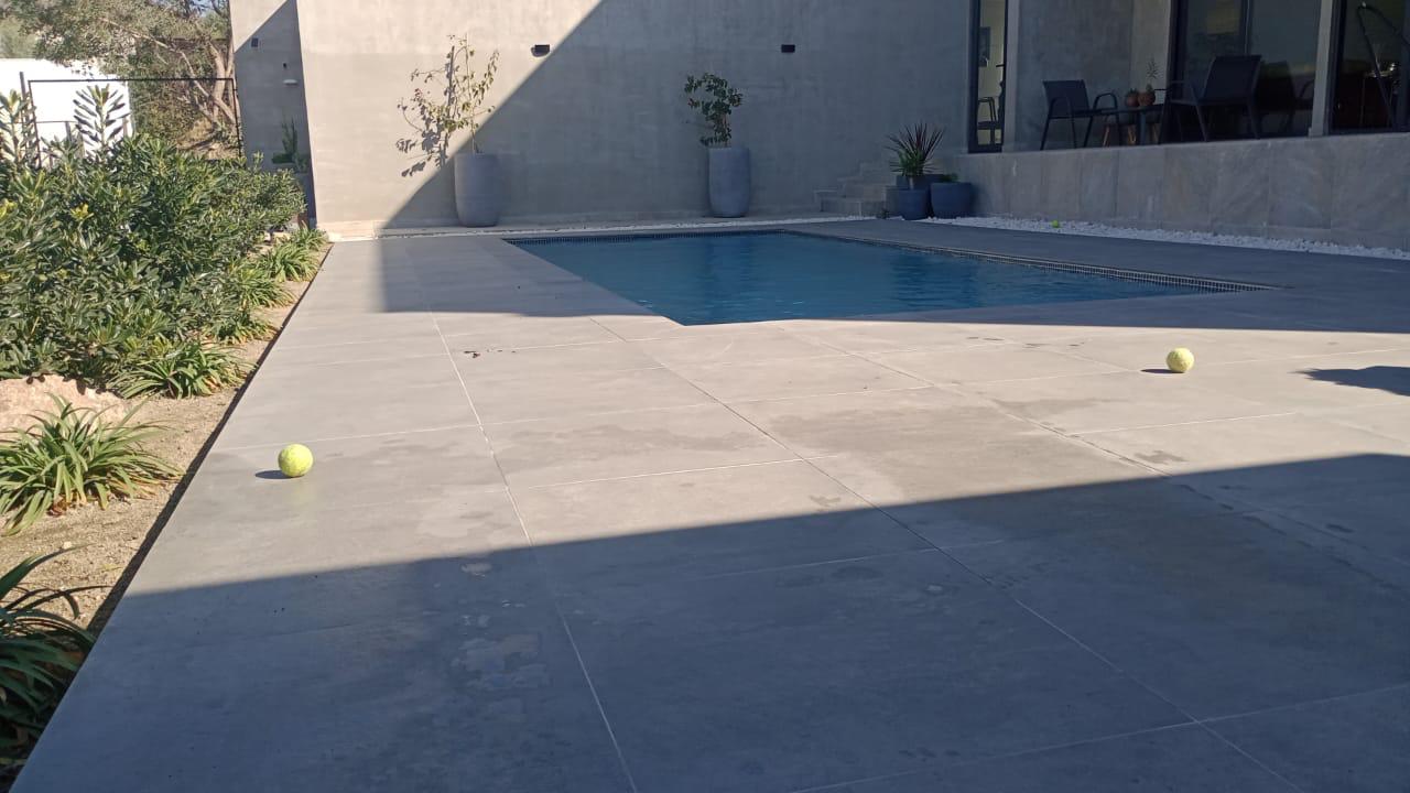 Piscina de línea minimalista con terraza de porcelanato gris junto a casa moderna