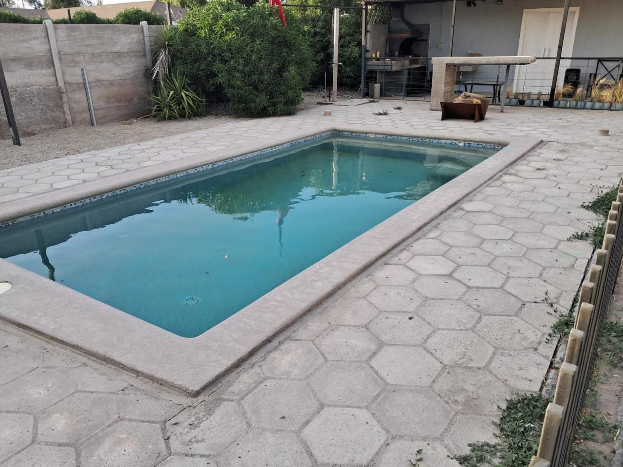 Piscina de hormigón con pavimento de pastelones hexagonales y quincho al fondo